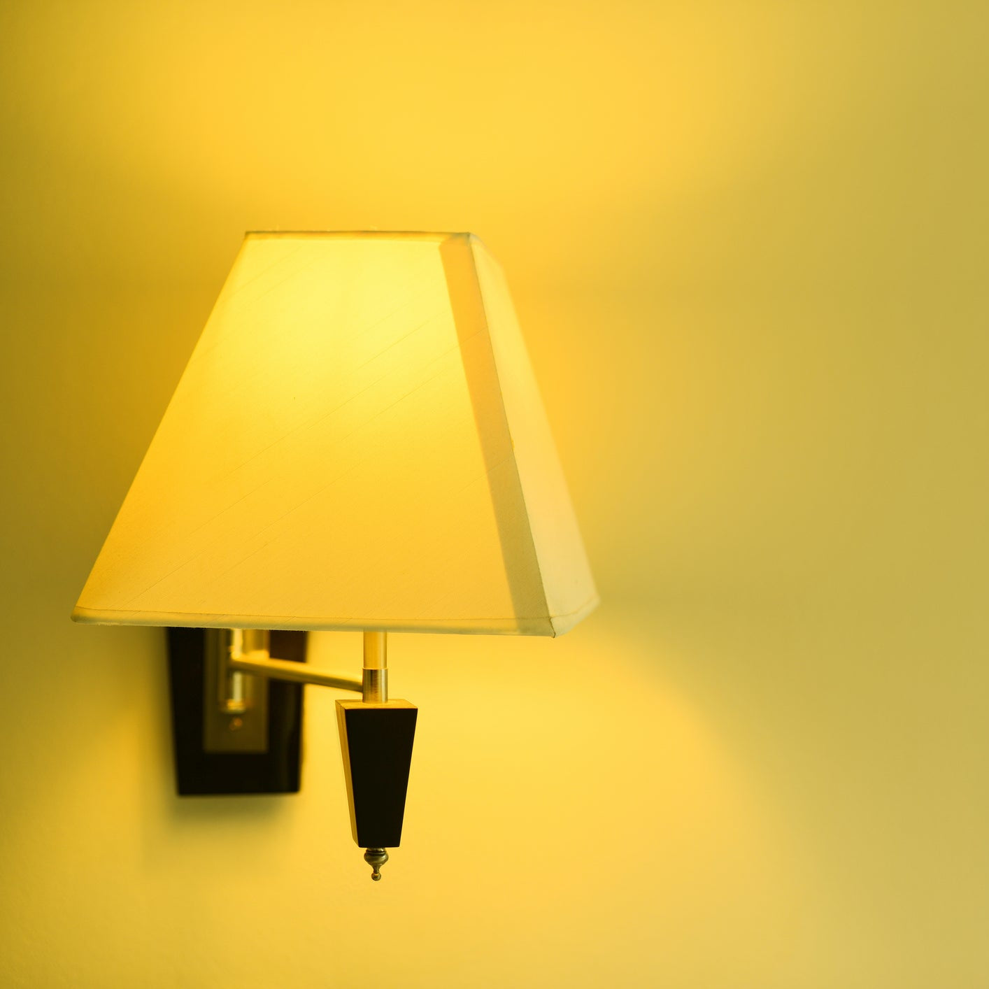 A white, basic rectangle-shaped lampshade with a hand rolled edge and a hard back with light on
